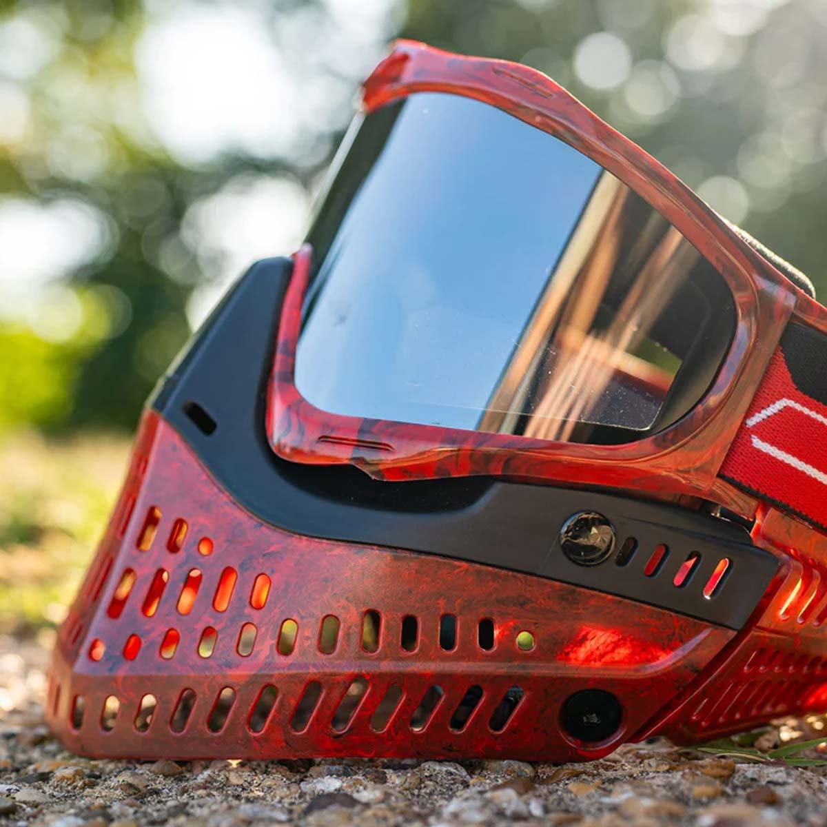 Red and black JT ProFlex Goggle LE Marble Red Black Home paintball mask with a smoke lens on an outdoor background