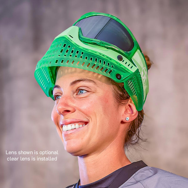 Person wearing a green JT ProFlex Birthstone Ice August Peridot paintball goggle with a smoke lens on a blurred background