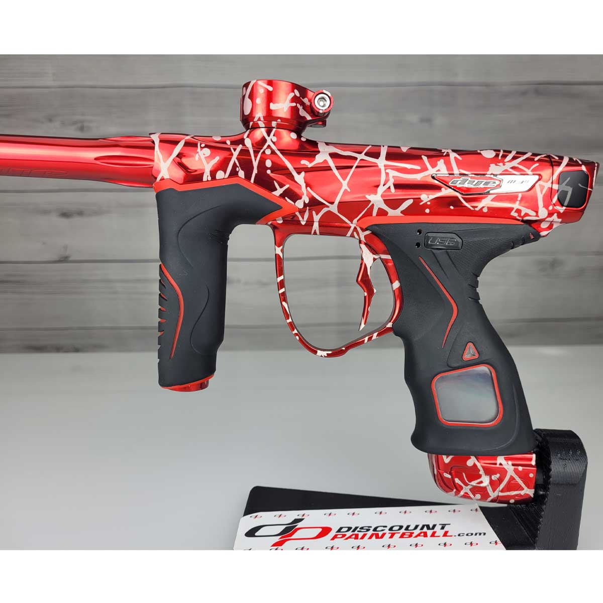 Left side body USED Red and black with white splash pattern Dye M3+ Paintball Marker Red Splash on a woodgrain background.