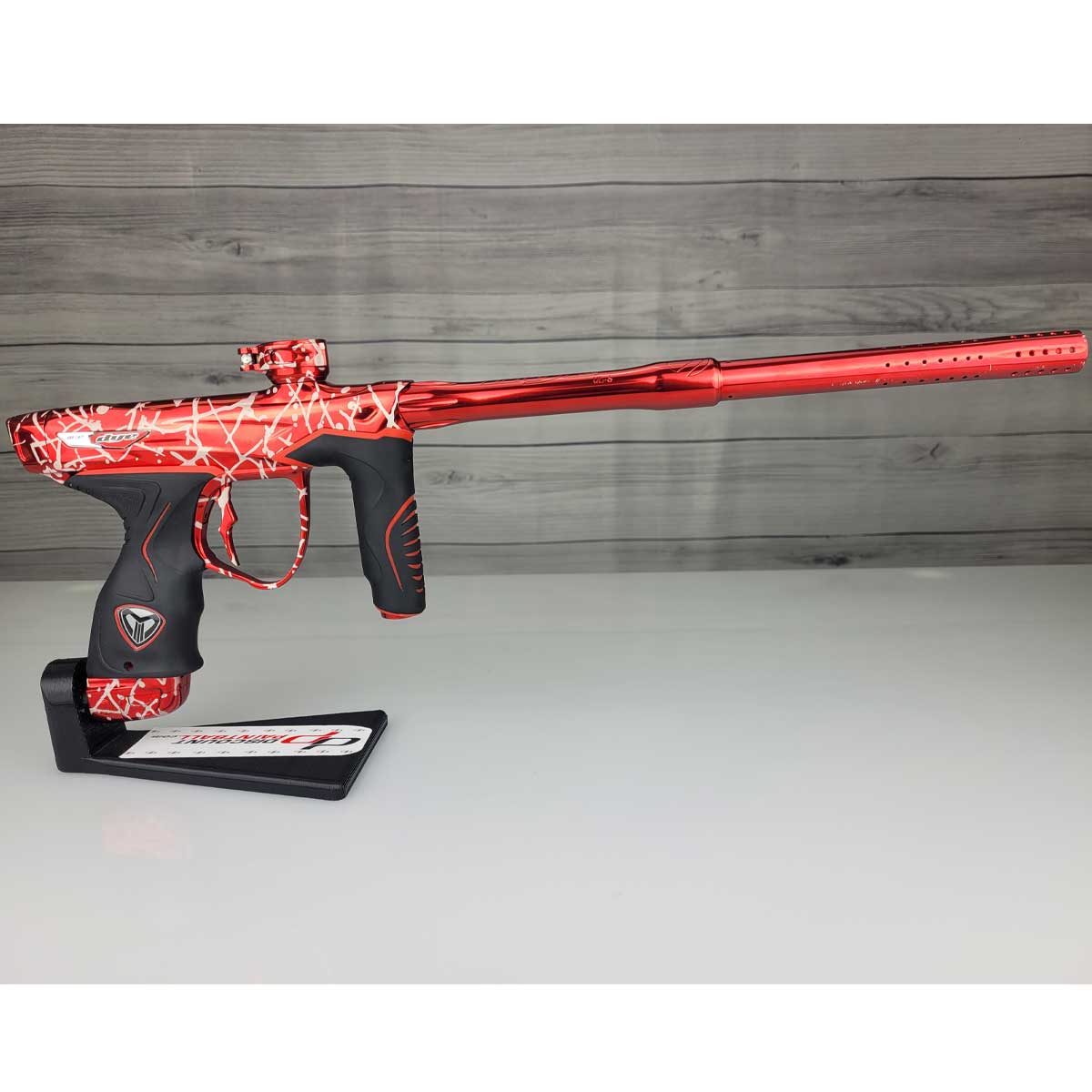 right side USED Red and black with white splash pattern Dye M3+ Paintball Marker Red Splash on a woodgrain background.