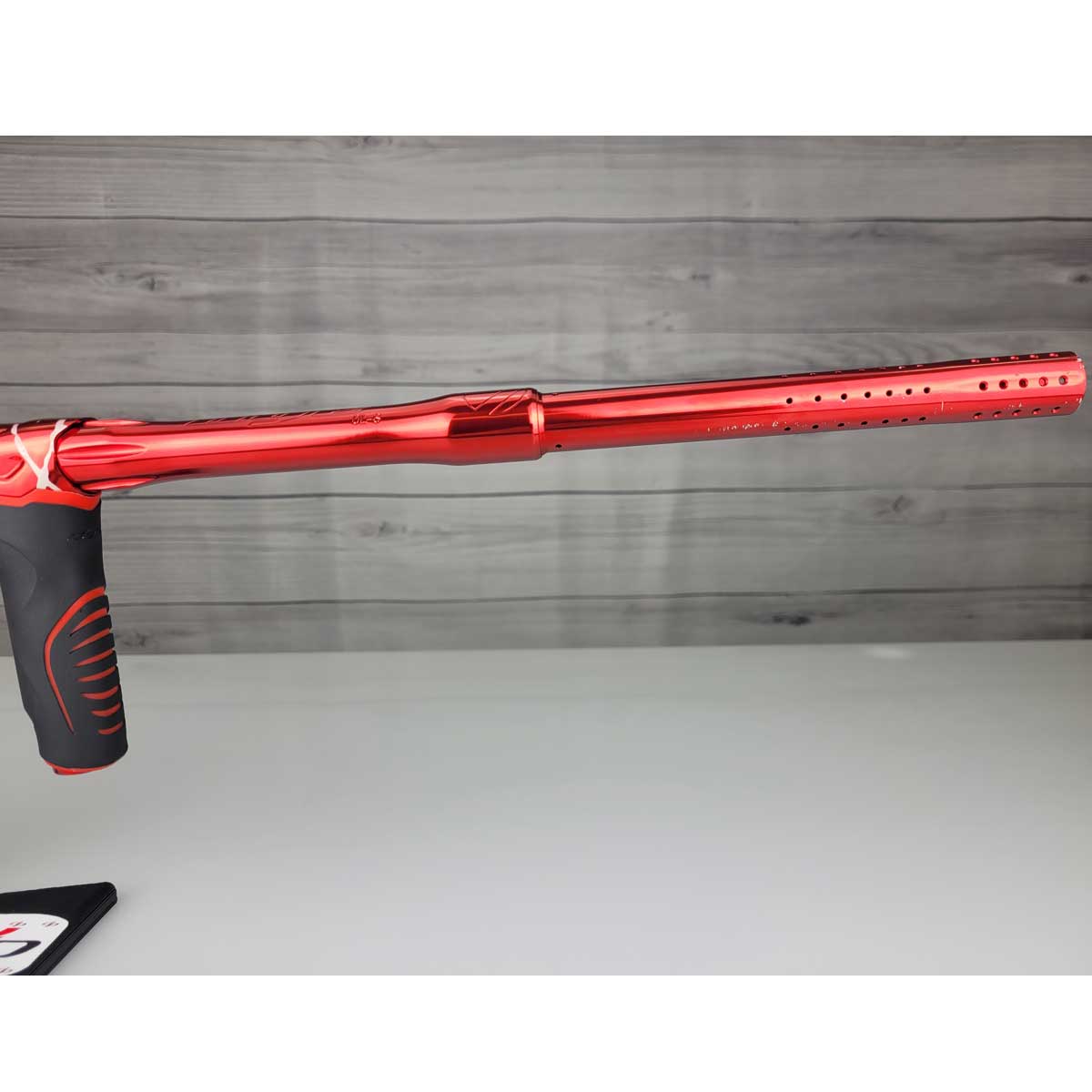 Rights side barrel USED Red and black with white splash pattern Dye M3+ Paintball Marker Red Splash on a woodgrain background.