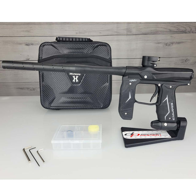 Left side USED Empire Axe 2.0 Paintball Marker Black with case and tools on a woodgrain background