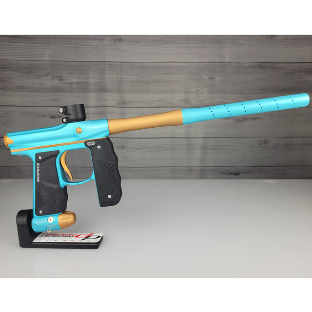 Blue and gold paintball gun on a white surface with a wooden background