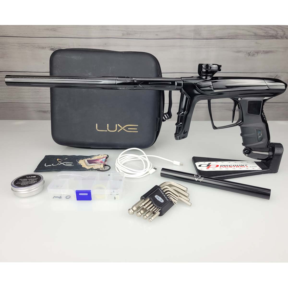 USED DLX Luxe IDOL Paintball Marker Black Polished with case with broken zipper and accessories on a woodgrain background
