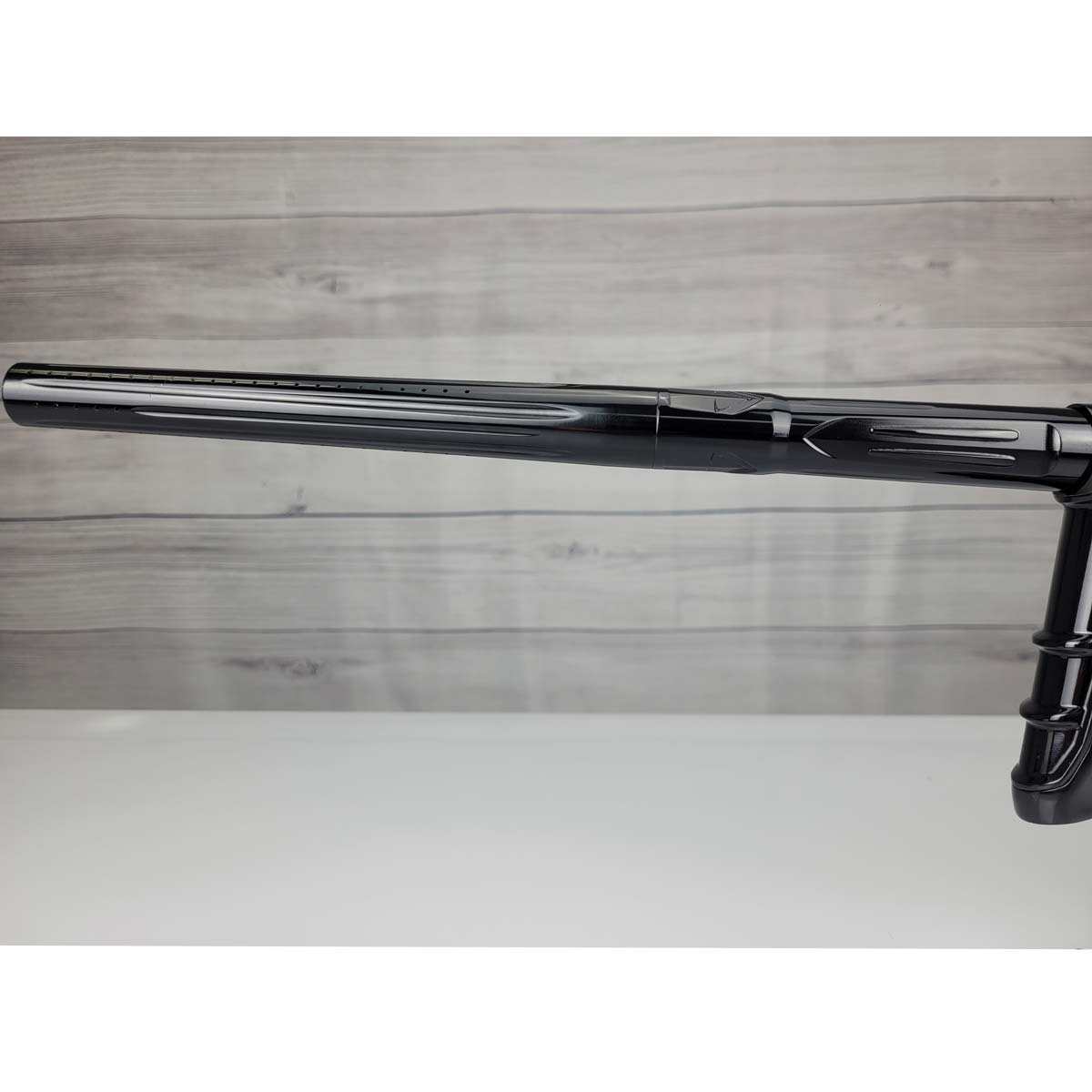 Left side barrel USED DLX Luxe IDOL Paintball Marker Black Polished on a woodgrain background