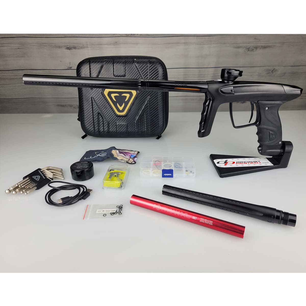 USED DLX Luxe TM40 Paintball Marker Black with case, parts and inserts against a woodgrain background