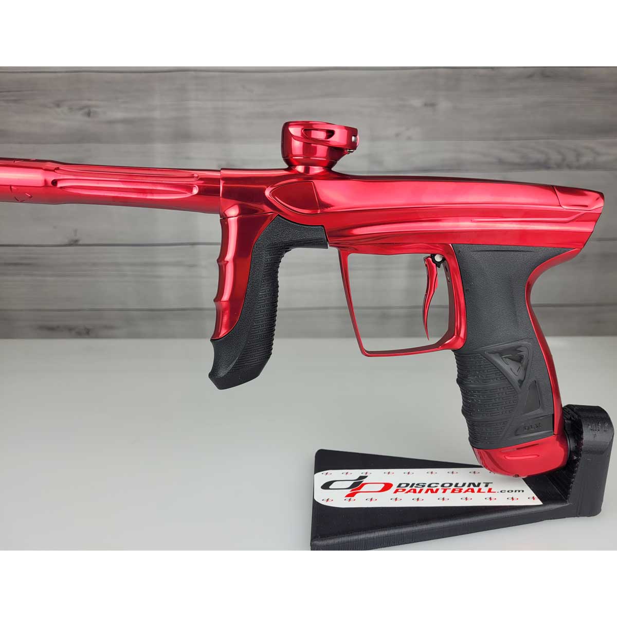 Left side body USED DLX Luxe Aire Red Polished paintball marker on a stand against a woodgrain background