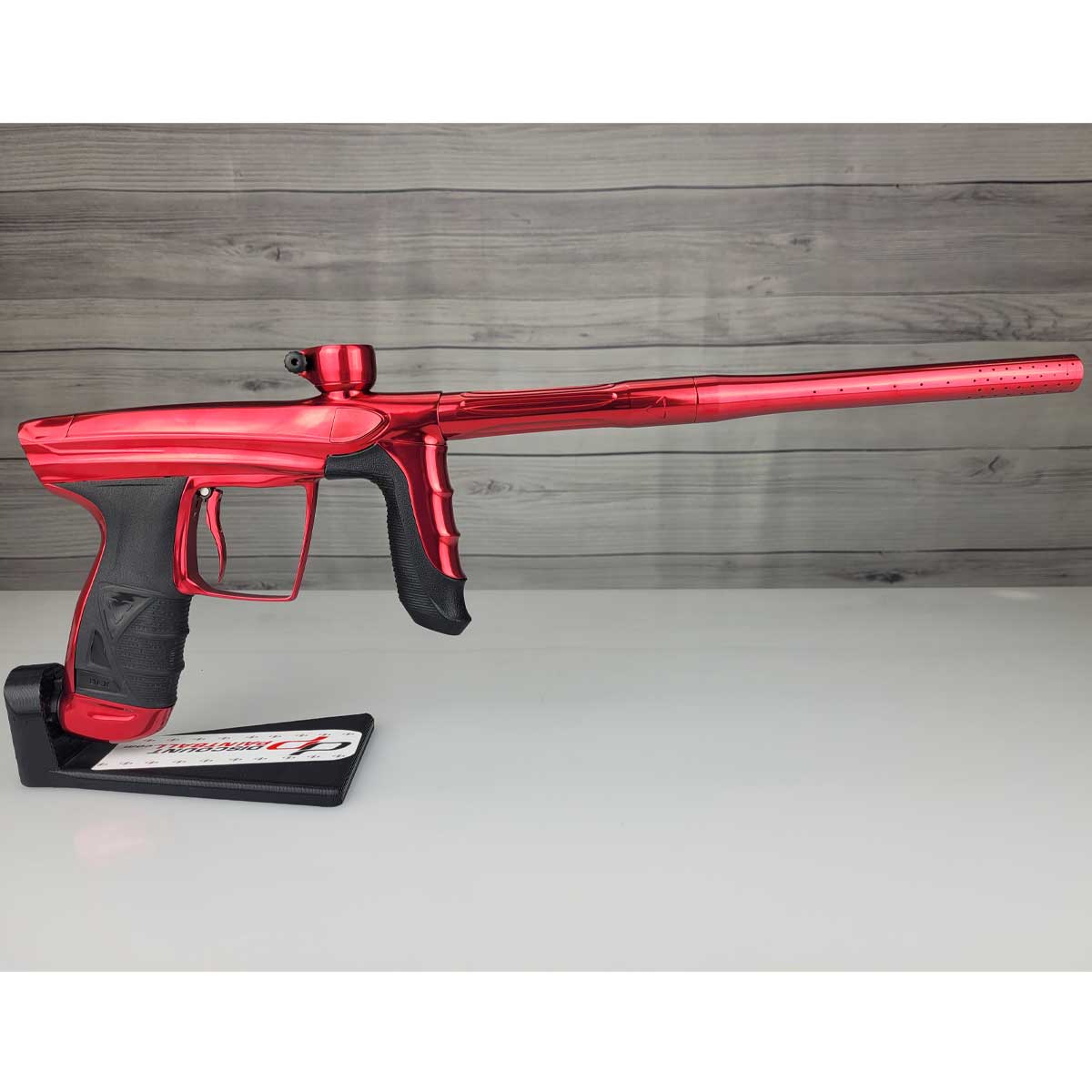 Right side USED DLX Luxe Aire Red Polished paintball marker on a stand against a woodgrain background