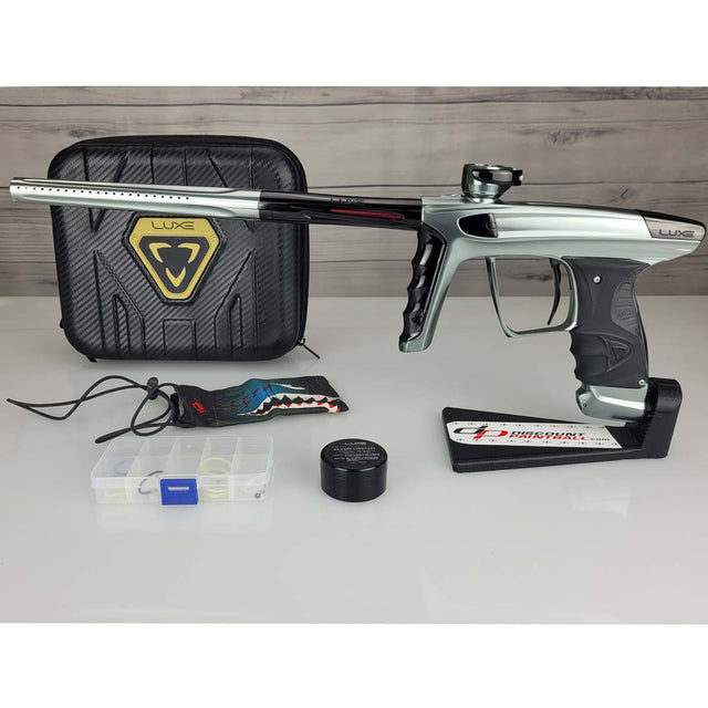 USED DLX Luxe X Silver Black Paintball marker with case and accessories on a white surface.
