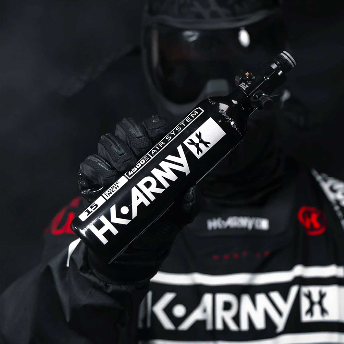 Black and white HK Army 15ci 4500psi Aluminum Compressed Air Tank for paintball or airsoft in a persons hand on a dark background