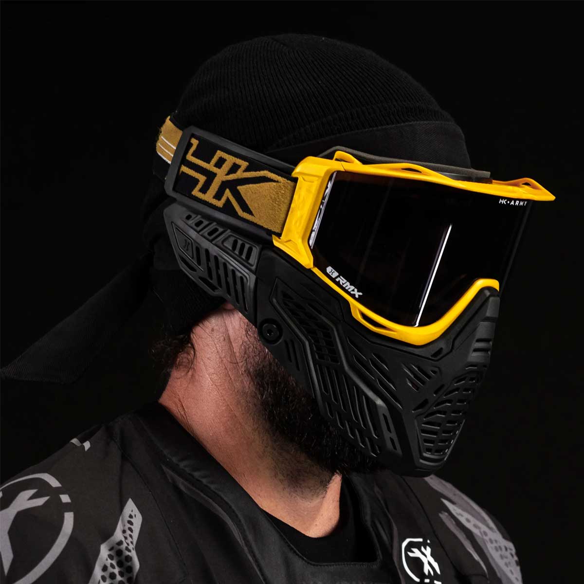 Side angle of person wearing HK Army RMX Thermal Paintball Goggles Black yellow Gold with smoke lens on a black background