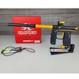 USED Empire Mini GS Black Gold Paintball marker with yellow accents and Empire Paintball branding on a red box and gray surface.