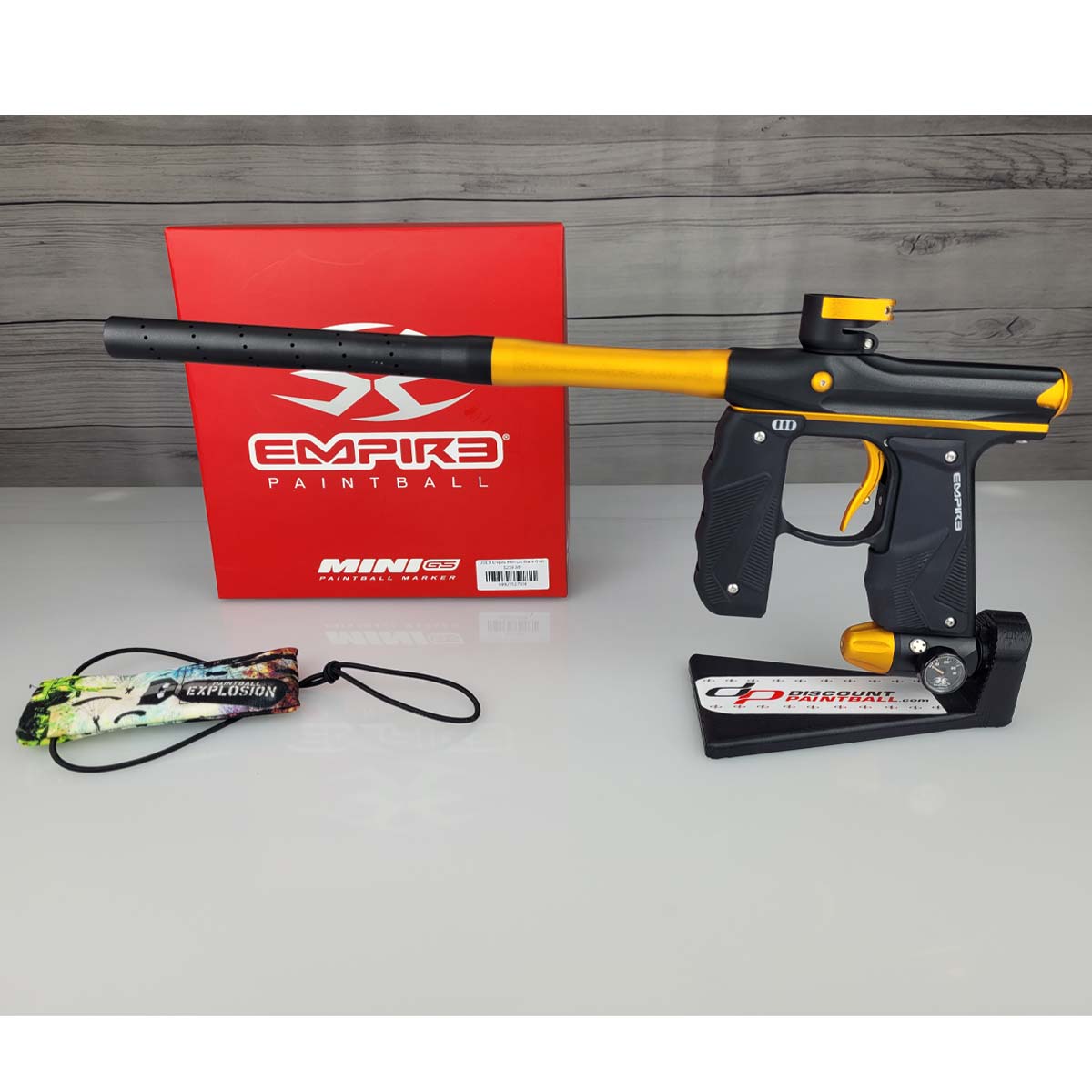 USED Empire Mini GS Black Gold Paintball marker with yellow accents and Empire Paintball branding on a red box and gray surface.