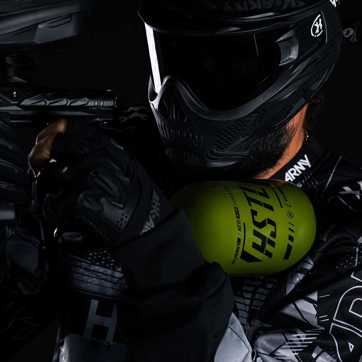 Paintball player holding the Olive HK Army HSTL 68ci 4500psi Compressed Air Tank mounted in marker