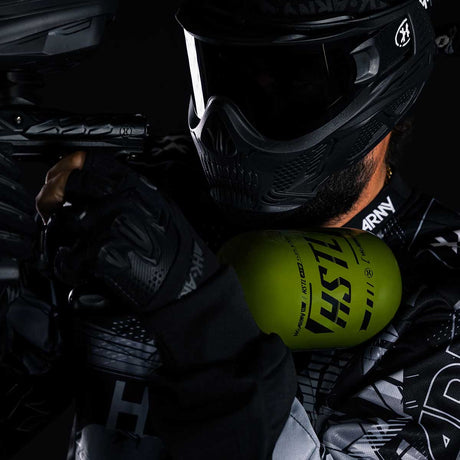 Paintball player holding the Olive HK Army HSTL 68ci 4500psi Compressed Air Tank mounted in marker