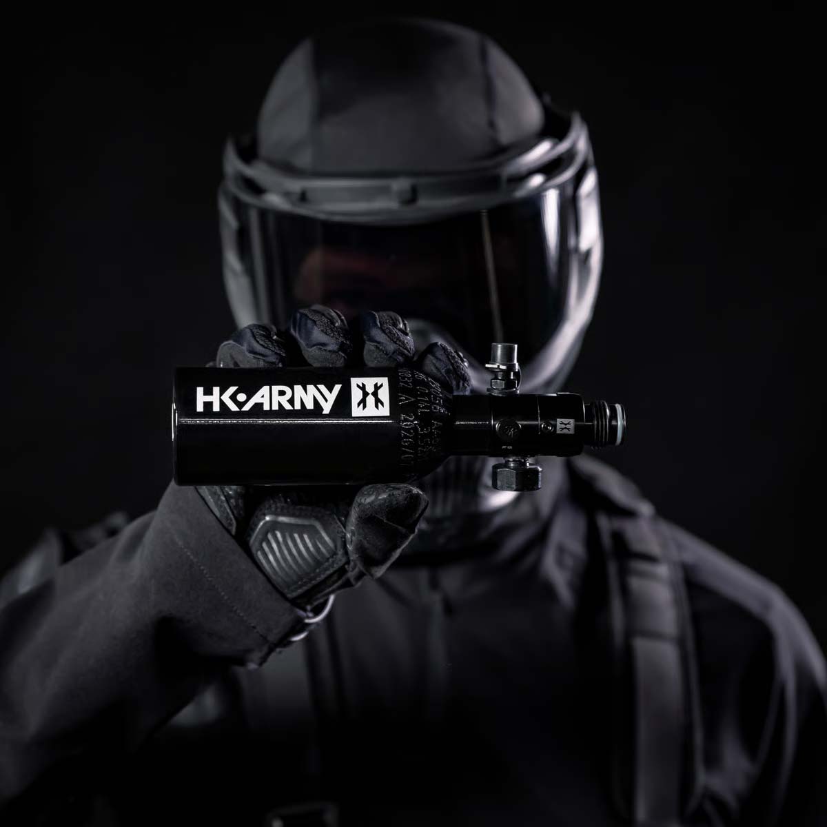 A black aluminum HK Army 9ci 3000 PSI high pressure tank with a black regulator being held by a person dressed for paintball or airsoft.