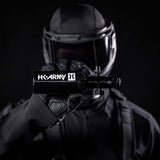 A black aluminum HK Army 9ci 3000 PSI high pressure tank with a black regulator being held by a person dressed for paintball or airsoft.
