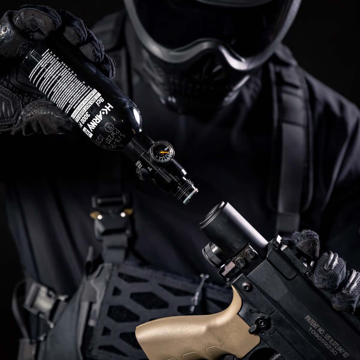 A black aluminum HK Army 9ci 3000 PSI high pressure tank with a black regulator shown with a launcher being held with a person.