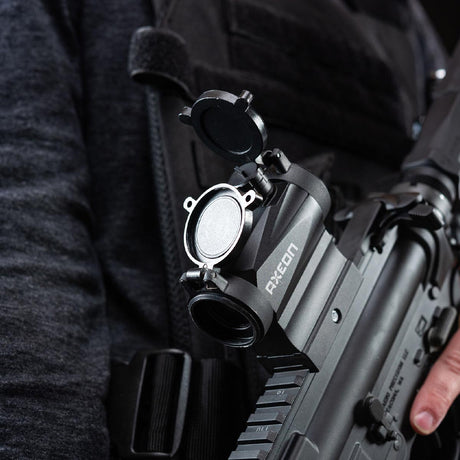 Left side view black AXEON 7XRGB20 Optic Tri Color Dot Sight mounted on a rifle being held by a person.