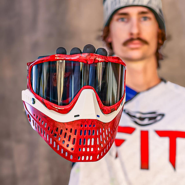 Red and white protective mask held by a person wearing a white shirt with red text.