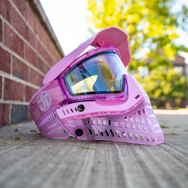 Pink JT ProFlex Birthstone Ice October Opal Goggle paintball mask on a concrete surface with a blurred outdoor background