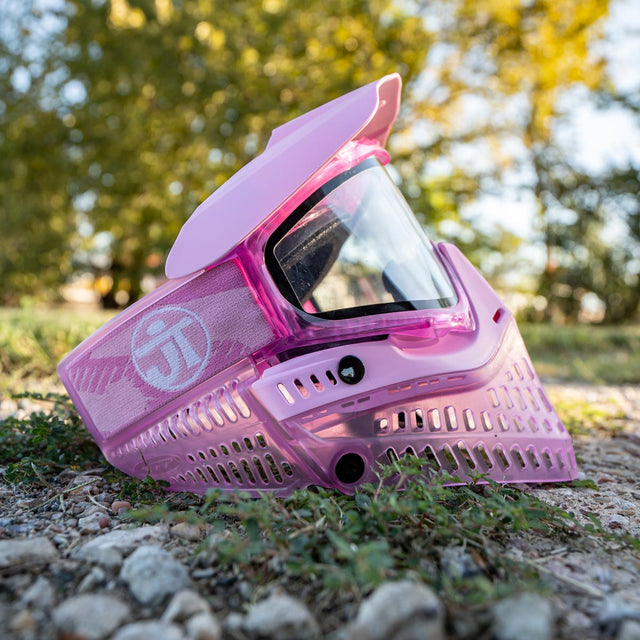 Pink JT ProFlex Birthstone Ice October Opal Goggle paintball mask on the ground with a blurred natural background
