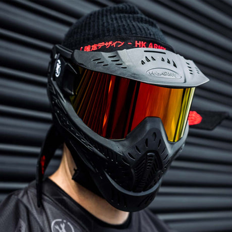 Black HK Army HSTL Thermal Paintball Goggle mask with a fire red lens and white AH logo on the side on a person against a black background.