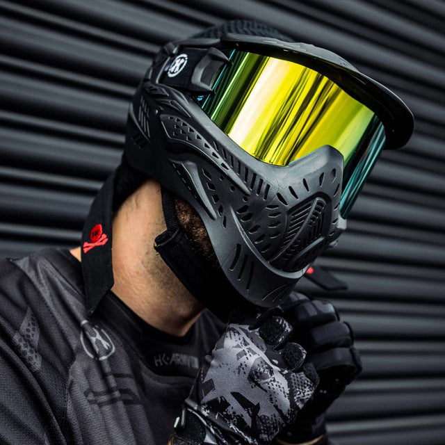 Black HK Army HSTL Thermal Paintball Goggle mask with a gold lens and white AH logo on the side shown on a person. 