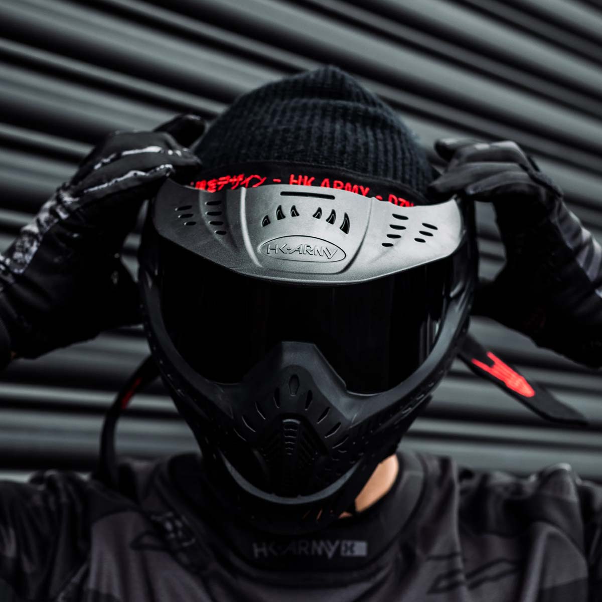 Black HK Army HSTL Thermal Paintball Goggle mask with a smoke lens and white AK logo on the side, shown on a person adjusting the goggle.