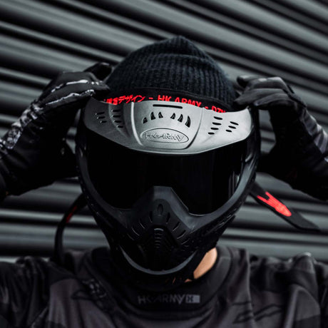 Black HK Army HSTL Thermal Paintball Goggle mask with a smoke lens and white AH logo on the side, shown on a person adjusting the goggle.
