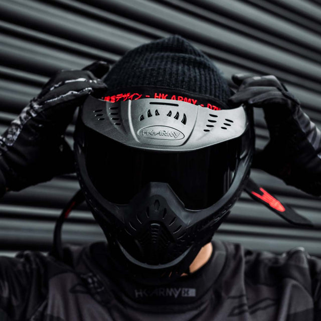 Black HK Army HSTL Thermal Paintball Goggle mask with a smoke lens and white AH logo on the side, shown on a person adjusting the goggle.