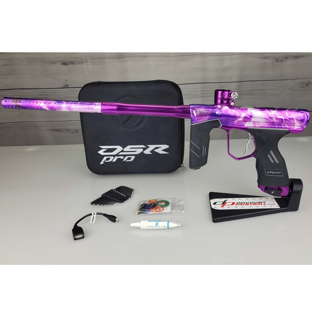 USED DYE DSR Pro PGA Grimace Purple Splash with case, tools, o rings, lube and cable against a wood panel background.