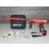 USED Red and black with white splash pattern Dye M3+ Paintball Marker Red Splash with case and spare parts kit on a woodgrain background.