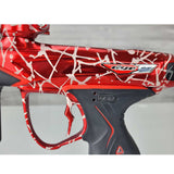 Close up of USB port cover USED Red and black with white splash pattern Dye M3+ Paintball Marker Red Splash on a woodgrain background.