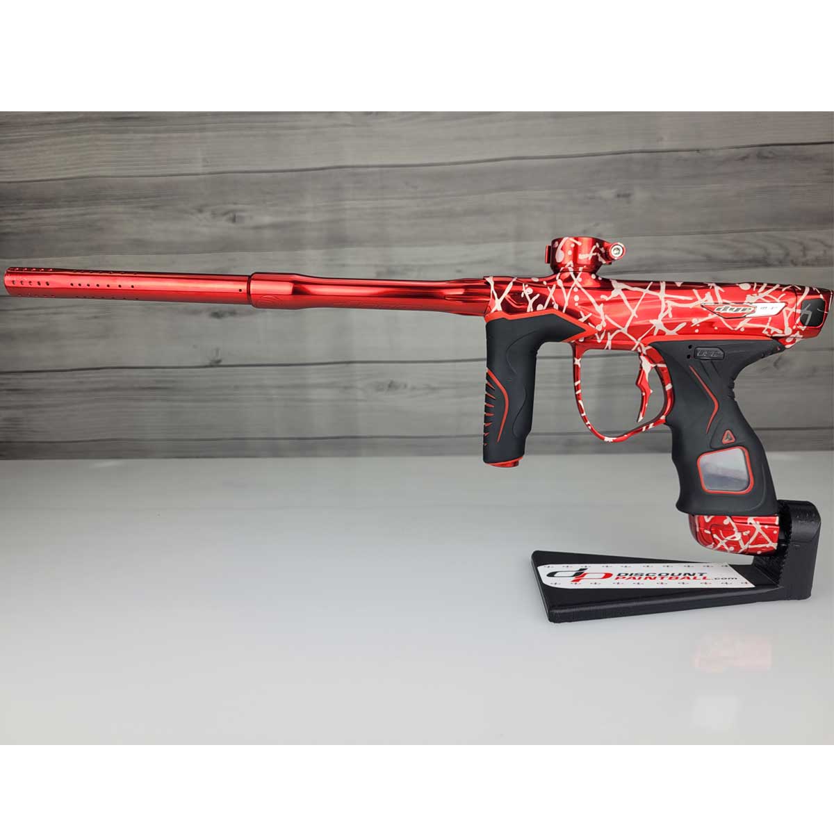 Left side USED Red and black with white splash pattern Dye M3+ Paintball Marker Red Splash on a woodgrain background.
