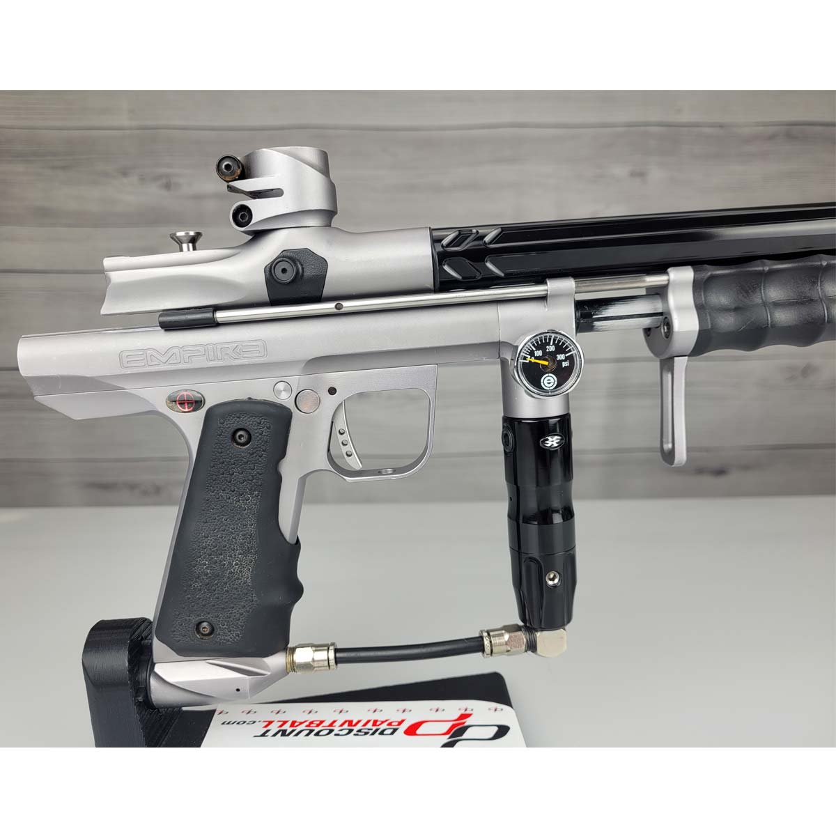 Right side body USED Empire Sniper Pump Grey paintball marker with a black and silver design on a white surface with a wooden background