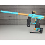 Blue and gold paintball gun on a gray surface with a wooden background