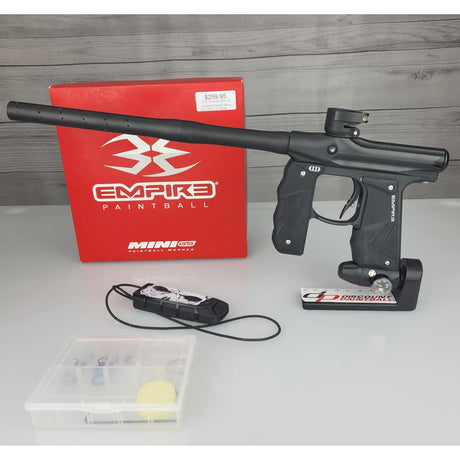 Black Empire Mini paintball gun with accessories on a gray surface, featuring Empire Paintball branding.