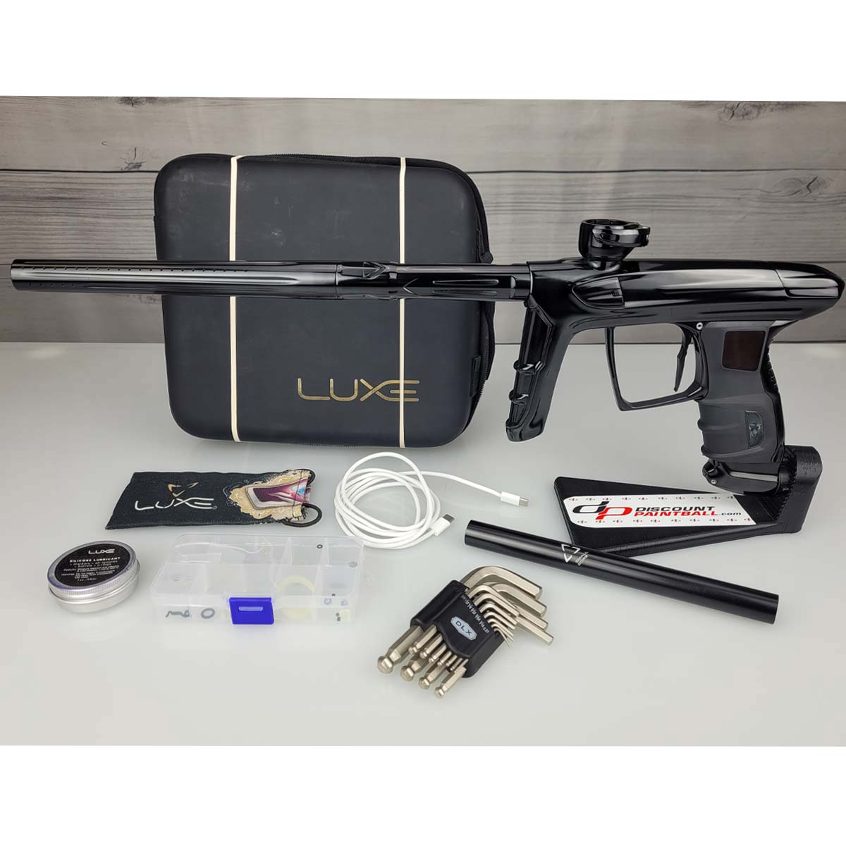 USED DLX Luxe IDOL Paintball Marker Black Polished with case and accessories on a woodgrain background
