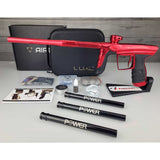 Left side USED DLX Luxe Aire Red Polished paintball marker on a stand with box, case, manual, barrel sock, 3 PWR inserts, tools and parts against a woodgrain background