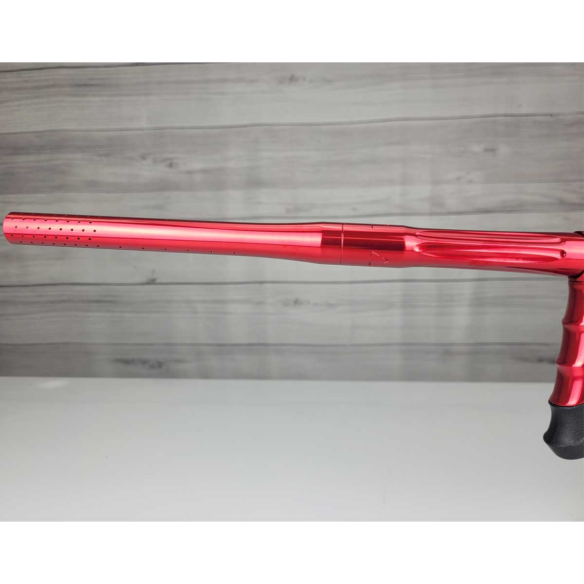 Left side barrel USED DLX Luxe Aire Red Polished paintball marker on a stand against a woodgrain background
