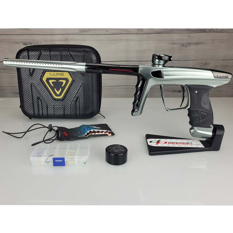 USED DLX Luxe X Silver Black Paintball marker with case and accessories on a white surface.