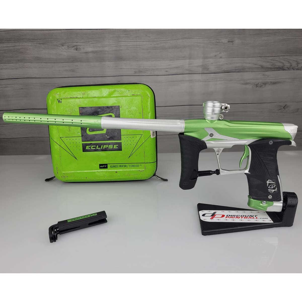 Green and silver USED Planet Eclipse Geo 3.5 Kyrpton Ice Green Silver paintball marker with green case and a set of hex keys on a wood panel background.