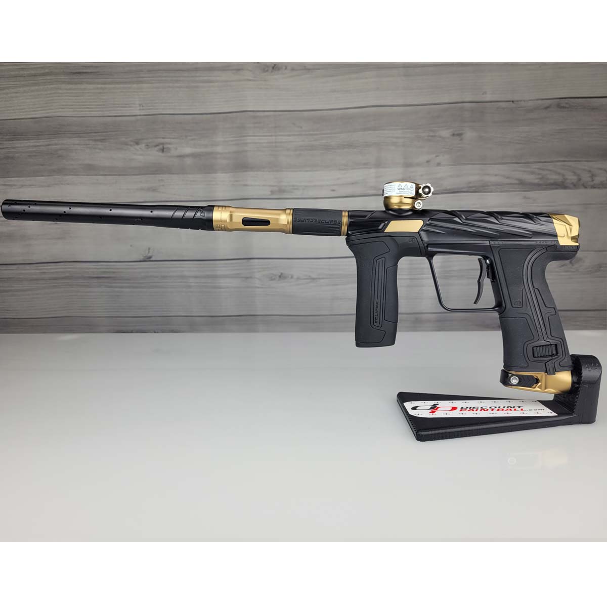 Black and gold USED Planet Eclipse Infamous CS3 paintball marker on a white surface with a wooden background