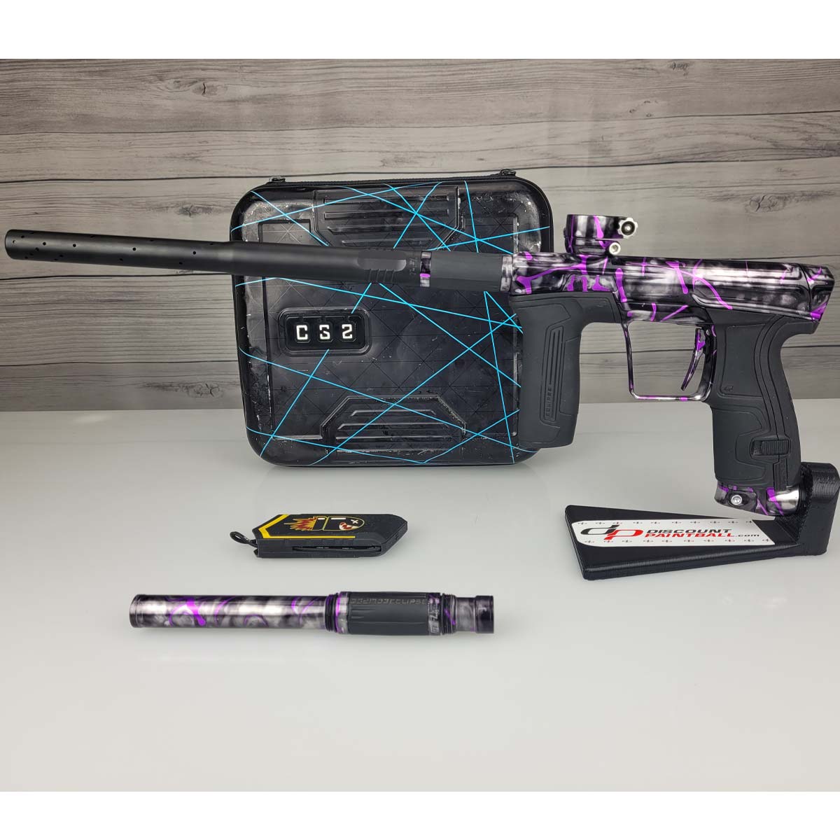 Left side USED Planet Eclipse CS2 Paintball Marker Black Purple Grey Splash with case and barrel sock and second barrel back on a woodgrain background