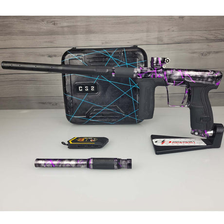 Left side USED Planet Eclipse CS2 Paintball Marker Black Purple Grey Splash with case and barrel sock and second barrel back on a woodgrain background