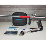 USED Shocker Era Paintball Marker Gray Red w case with accessories on a white surface and wooden background
