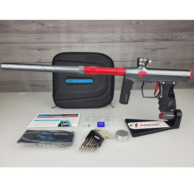 USED Shocker Era Paintball Marker Gray Red w case with accessories on a white surface and wooden background