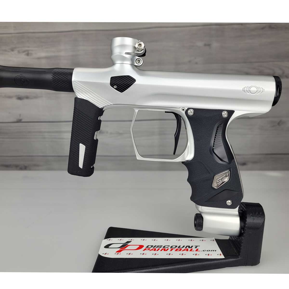Left side body USED Shocker Era Silver black paintball marker in a stand on a woodgrain background.
