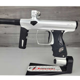 Left side body USED Shocker Era Silver black paintball marker in a stand on a woodgrain background.